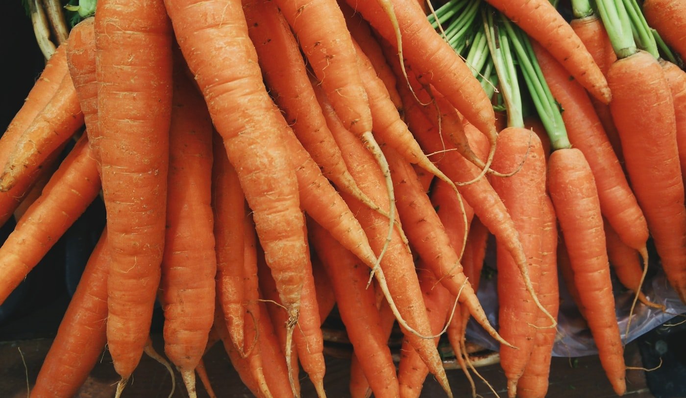 Fresh carrots with their green tops, laid out on a wooden surface